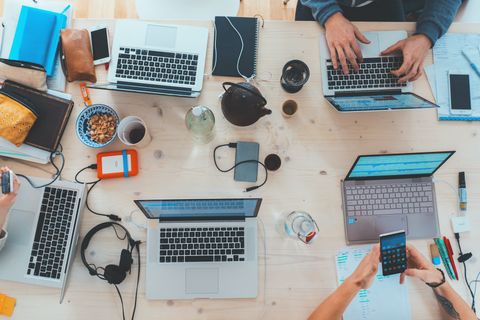 People gathered around a table with multiple computers, cellphones, and
notebooks on top.
